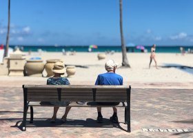 senior couple sitting on a bench facing a beach